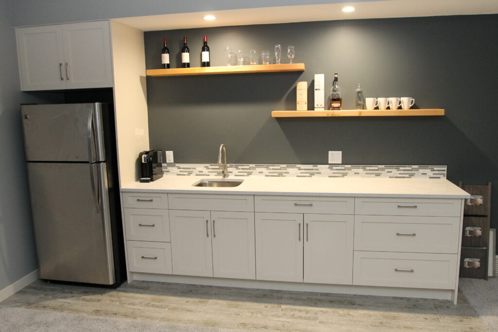 Custom-built white cabinetry and floating wood shelves in a basement kitchenette